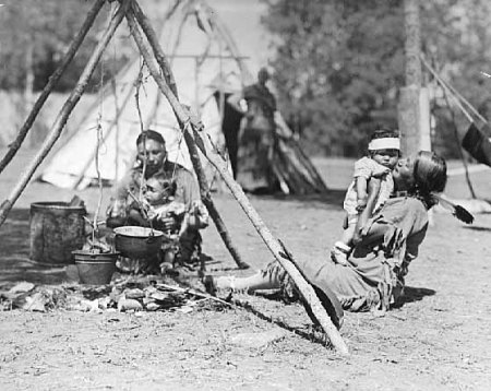 women and children seated by camp fire in Chippewa village, Itasca State Park